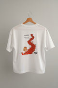 A white short-sleeve t-shirt hanging on a wooden hanger against a beige wall. The shirt features a graphic print of a the nut character and squirrel path in Arosa and black text.