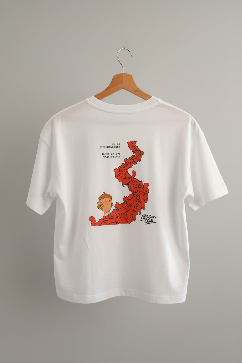 A white short-sleeve t-shirt hanging on a wooden hanger against a beige wall. The shirt features a graphic print of a the nut character and squirrel path in Arosa and black text.