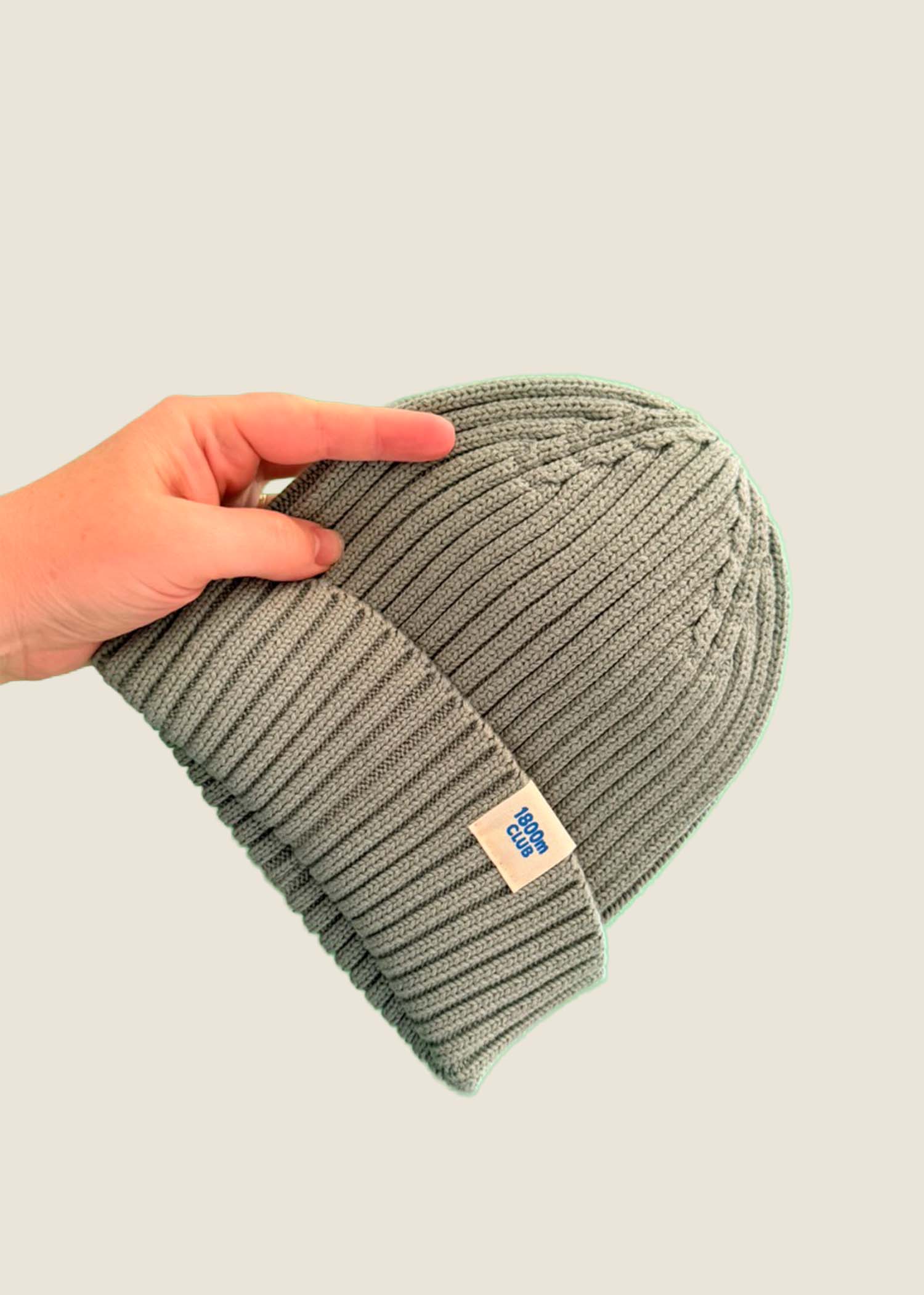 Sage green ribbed kids’ beanie with cream 1800m Club label. Made in Arosa, Switzerland.