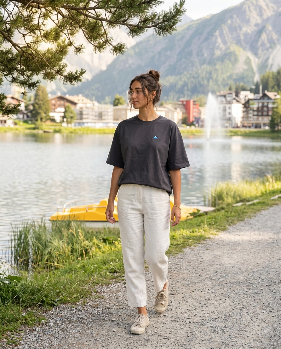 A woman walking along the Arosa Obersee wearing the 1800m Club Hörnli embroidered Boxy T-shirt designed in Arosa, Switzerland.